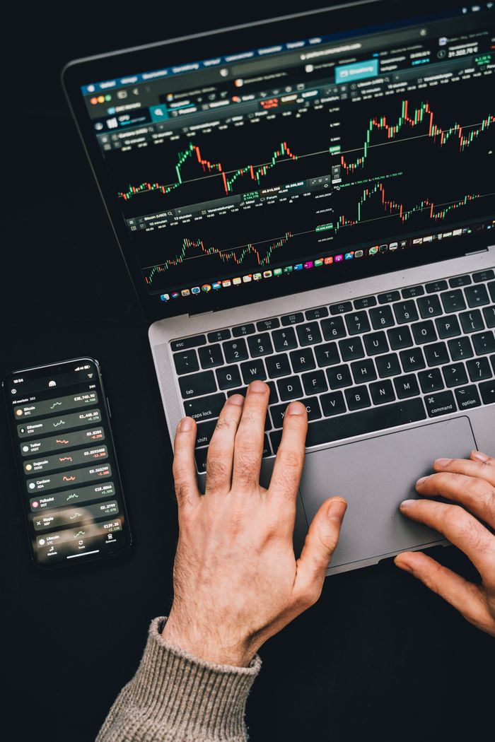 creative-03 Hands typing on a laptop with cryptocurrency charts and smartphone display in view, focusing on digital finance.